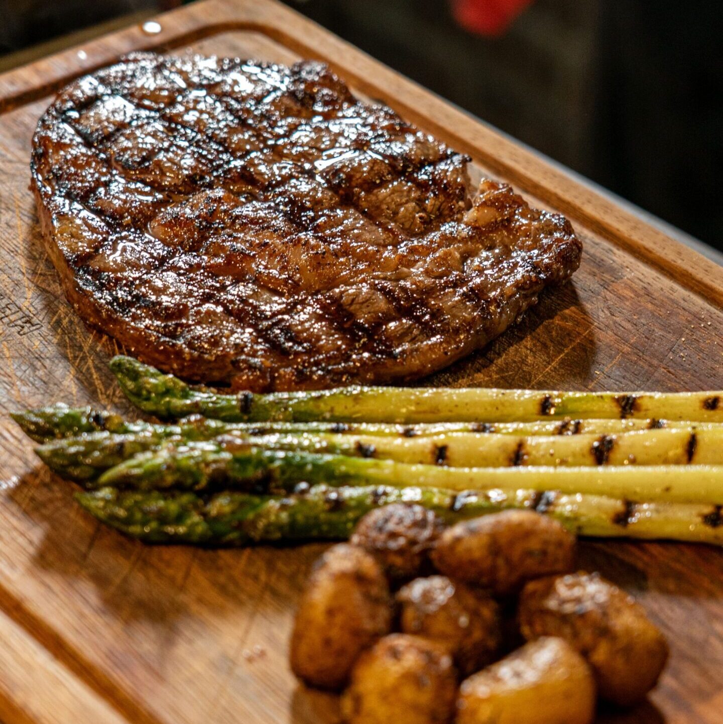 Grilled steak with asparagus and roasted potatoes on wooden board.